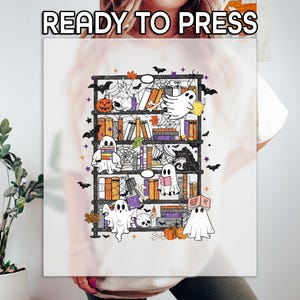 May include: White t-shirt with a Halloween-themed graphic. The design features a bookshelf filled with books, ghosts, pumpkins, bats, and spiderwebs. The text "READY TO PRESS" is at the top.