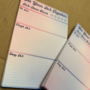 May include: Two pink and blue gradient notepad sets with the text "Get Your Shit Together" and "Shit-Show Level" with a five-star rating system. The notepad is divided into three sections: "Oh Shit", "Tough Shit", and "Easy Shit".
