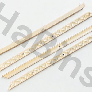 May include: Four beige plastic picture frame hanging strips. Two strips have a series of triangular patterns along the edge. The other two strips are plain. All strips have small holes and are angled at the ends.