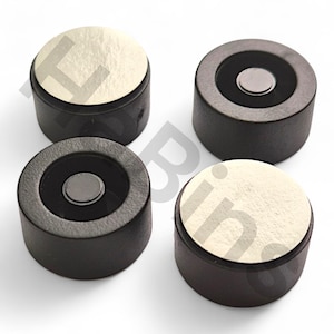 以下が含まれることがあります： 円形の明るい色の上面を持つ、4つの小さな円筒形の黒い物体。2つは銀色の中心を持ち、2つは白いテクスチャ加工された上面を持っています。物体は均等に配置されており、磁石または同様のコンポーネントのようです。