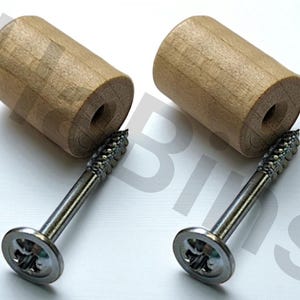 Może przedstawiać: Dwa drewniane kołki meblowe o cylindrycznym kształcie, każdy w połączeniu ze srebrną śrubą. Kołki są jasnobrązowe i mają centralny otwór. Śruby mają płaską główkę z krzyżowym wgłębieniem.