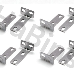 Może przedstawiać: Osiem srebrnych metalowych wsporników narożnych na białym tle. Każdy wspornik ma kształt kąta prostego z dwoma otworami montażowymi. Wsporniki wydają się nowe i nieużywane.