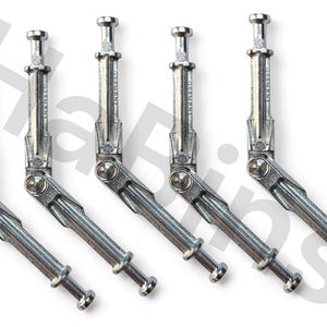 Może przedstawiać: Zestaw pięciu srebrnych, przegubowych zawiasów metalowych. Każdy zawias ma cylindryczne kołki na końcach i centralny przegub obrotowy. Widoczny napis "GERMANY". Ułożone po przekątnej na białym tle. Do mebli.