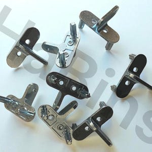 Puede incluir: Un surtido de conectores metálicos plateados para muebles. Cada conector tiene un diseño en forma de T con una parte superior plana, un brazo perpendicular y múltiples postes cilíndricos para la fijación. Los conectores están dispersos sobre una superficie blanca.