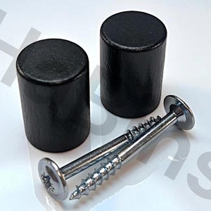 May include: Two black wooden cylindrical furniture knobs with a textured surface are displayed next to two silver screws. The knobs are approximately 1.5 inches tall and 1 inch in diameter. The screws have a flat head.