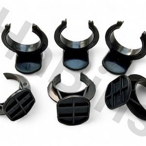 May include: A collection of six black plastic clips, each featuring a curved, C-shaped design with a flat base. The clips are arranged on a white surface, showcasing their form and structure. The bases have a grid-like pattern.