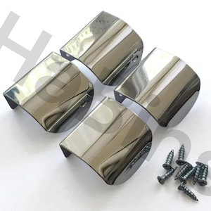 Puede incluir: Cuatro tiradores de armario cromados con un diseño curvo, dispuestos sobre una superficie blanca. Un pequeño montón de tornillos negros está junto a los tiradores. Estas piezas de ferretería son probablemente para muebles o armarios.