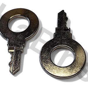 Könnte beinhalten: Zwei silberfarbene Schlüssel mit kreisförmigen Griffen und unterschiedlichen Bartdesigns. Die Schlüssel sind wahrscheinlich für einen bestimmten Schlosstyp, mit einem Schlüssel mit detailliertem Bartmuster und einem einfacheren Design.