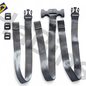 Op de afbeelding: Een assortiment zwarte en grijze riemen en gespen, waarschijnlijk voor meubels of om items vast te zetten. De set bevat meerdere riemen met verstelbare gespen, plus extra zwarte plastic onderdelen. Het IKEA-logo is zichtbaar.