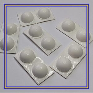 Op de afbeelding: Verschillende witte, koepelvormige objecten zijn gerangschikt op een licht oppervlak. Elk object is verpakt in een rechthoekige, witte plastic container met twee afgeronde compartimenten. De objecten lijken klein, mogelijk componenten of accessoires.