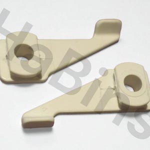 May include: Two beige plastic levers with a rectangular base and a curved arm. Each lever has a circular hole and a raised section at the end of the arm. The levers are positioned on a white surface.