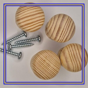 Op de afbeelding: Een verzameling van vier onafgewerkte houten kastknoppen met zichtbare houtnerf, samen met verschillende zilveren schroeven. De knoppen zijn rond en klaar voor installatie. Ideaal voor doe-het-zelf meubelprojecten of kastupgrades.