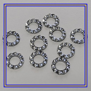May include: A collection of ten silver-colored, toothed lock washers. Each washer has a circular shape with a central hole and a series of teeth around the outer edge. The washers are scattered on a light-colored surface.