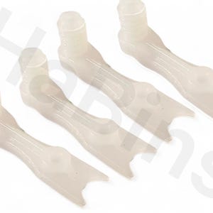 Może przedstawiać: Cztery białawe plastikowe elementy. Każdy element ma cylindryczną górę, długi, zakrzywiony korpus i rozwidczony koniec. Przedmioty są ułożone po przekątnej w ramie, z miękkim, rozproszonym oświetleniem.