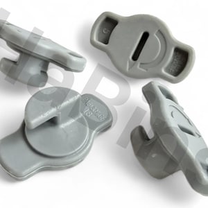 May include: Four gray plastic components, possibly automotive parts, are arranged on a white background. Each piece has a unique shape, with some featuring a hook or a circular design. The parts appear to be new and unused.