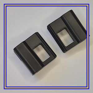 Puede incluir: Dos componentes rectangulares de plástico negro con un recorte rectangular en el centro. Los componentes están sobre un fondo blanco y enmarcados por un borde azul y amarillo.