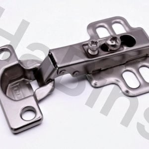 May include: A silver-colored cabinet hinge with a rectangular base and a pivoting arm. The hinge has two screw holes on the base and two on the mounting plate. The hinge is designed for use on cabinet doors and drawers.