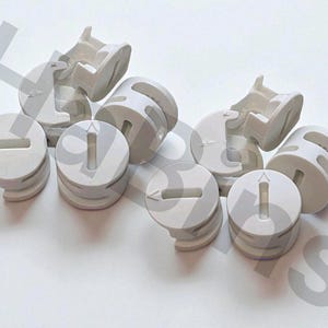 以下が含まれることがあります： ライトグレーの家具用カムロックと接続ボルトのコレクション。カムロックはスロットと矢印が付いた円形で、ボルトは湾曲したデザインです。これらのハードウェアは家具の組み立て用です。