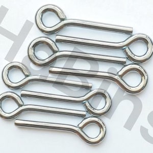 Puede incluir: Una colección de pasadores de chaveta brillantes de color plateado. Cada pasador tiene un ojo en bucle en un extremo y un vástago recto. Los pasadores están dispuestos sobre una superficie blanca, con las anillas orientadas en la misma dirección.