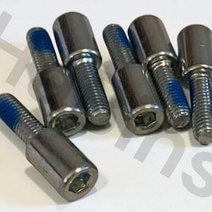 Puede incluir: Un conjunto de pernos plateados con fijador de roscas azul aplicado a las roscas. Los pernos tienen una cabeza hexagonal y un cuerpo cilíndrico. Los pernos están dispuestos sobre una superficie blanca.