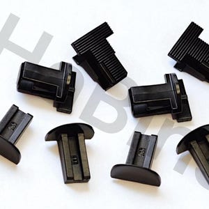 May include: An assortment of black plastic components, likely for a larger product. The pieces have a T-shaped design with a curved base and a rectangular top. Some tops have a ridged texture.