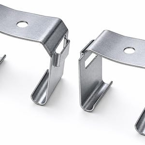May include: Two identical silver-colored metal mounting brackets with a U-shaped profile. Each bracket features a flat top surface with a centered circular hole and two rectangular side slots, with curved edges extending downward on both sides.
