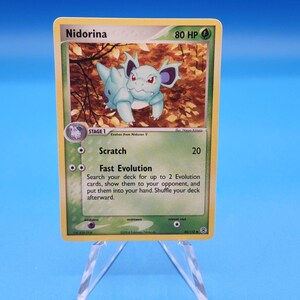 May include: A Nidorina trading card with 80 HP, featuring a light blue creature illustration against an autumn leaf background. The card text includes the attacks Scratch and Fast Evolution, with stage 1 status and a green border design.
