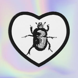 May include: Embroidered patch featuring a black beetle design within a white heart shape, outlined in black. The beetle has detailed legs and body features. The background has a soft, iridescent rainbow effect.