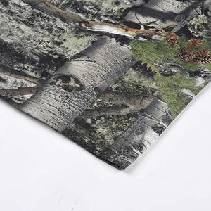 May include: Close-up of a camouflage fabric. The pattern incorporates greens, browns, and greys, resembling a woodland setting. The fabric's texture is evident, with details of tree bark and foliage.