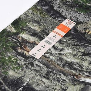 May include: Camouflage fabric in shades of green, brown, and grey, with a tag labelled "ADULT" and "SMALL". The pattern resembles a woodland scene. The tag includes a barcode and a brand logo.