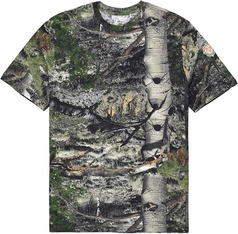 May include: A camouflage-patterned t-shirt with short sleeves, displaying a blend of green, brown, and grey hues, resembling a woodland scene. The shirt has a crew neck and a small logo patch on the sleeve.
