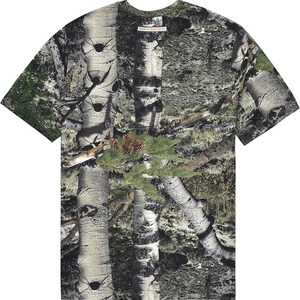May include: A short-sleeved t-shirt with a camouflage design incorporating birch tree bark, green foliage, and pine cones. The shirt has a crew neck and a tag that reads "GEAR UP, GEAR DOWN".