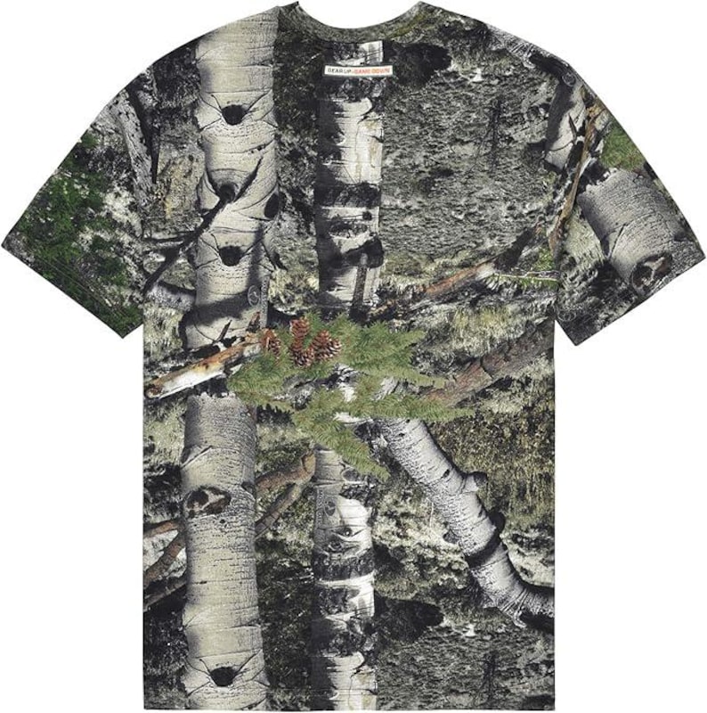May include: A short-sleeved t-shirt with a camouflage design incorporating birch tree bark, green foliage, and pine cones. The shirt has a crew neck and a tag that reads "GEAR UP, GEAR DOWN".