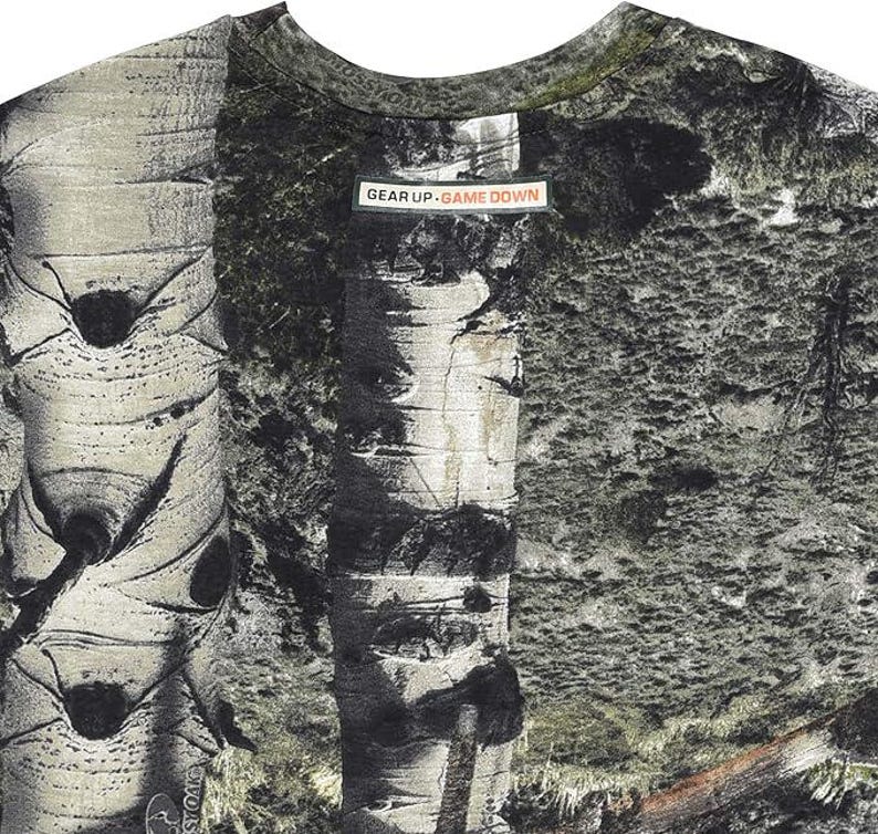 May include: A crew neck t-shirt with a nature-inspired design. The shirt features a detailed print of birch tree bark and foliage in shades of grey, green, and brown. The text "GEAR UP. GAME DOWN" is printed on a rectangular label.