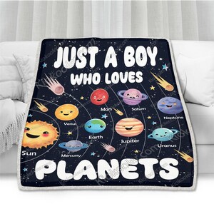May include: A black and blue fleece blanket with a white outline. The blanket features a graphic of the planets in our solar system with cartoon faces. The text "Just a boy who loves planets" is printed in white on the blanket.