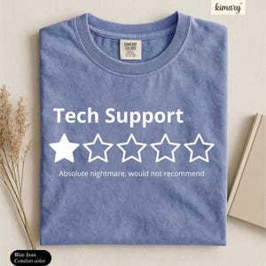 May include: A blue jean colored t-shirt featuring the white text Tech Support above a single solid white star and four white outlined stars. Below the stars, the white text reads Absolute nightmare, would not recommend. The shirt has a crew neckline.