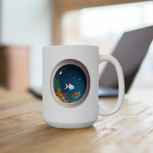 May include: White ceramic mug with a round, blue, and white image of a fish tank with two fish, coral, and seaweed. The mug has a white handle.