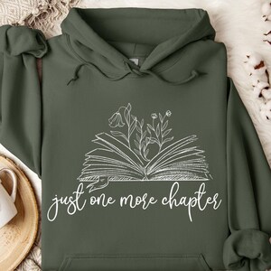 May include: A dark green hooded sweatshirt with a white graphic of an open book with flowers growing from it. The text "just one more chapter" is printed below the book.
