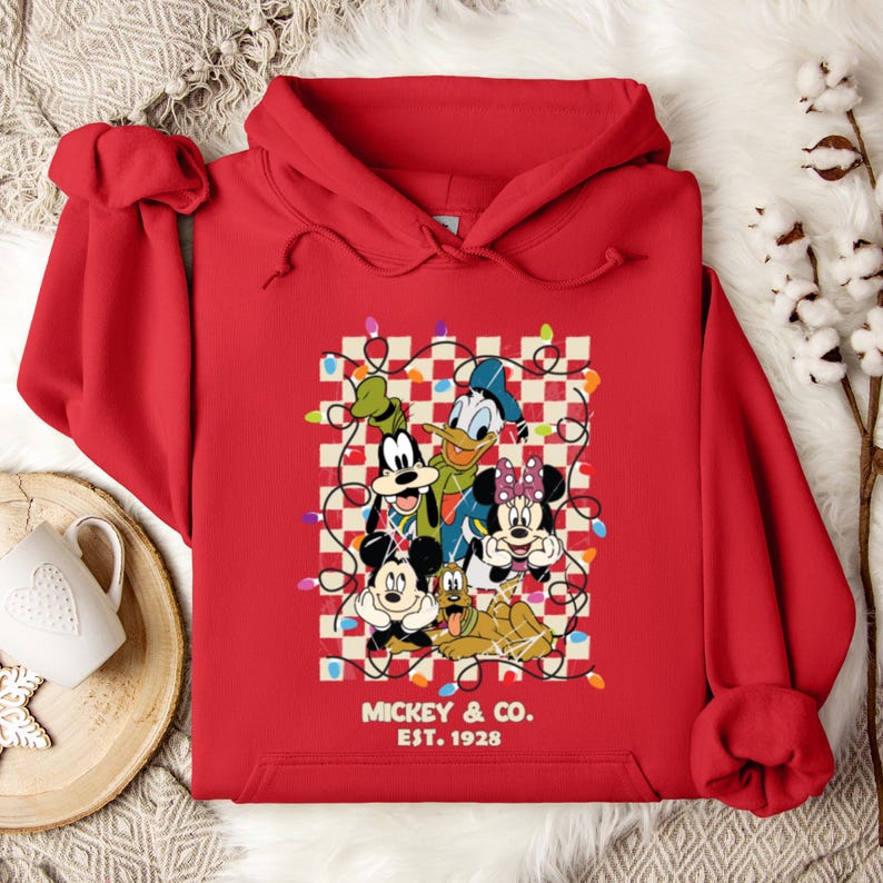 May include: Red hooded sweatshirt with a Christmas-themed graphic featuring Mickey Mouse, Minnie Mouse, Donald Duck, Goofy, and Pluto. The graphic includes a checkered background with string lights and the text "Mickey & Co. Est. 1928".