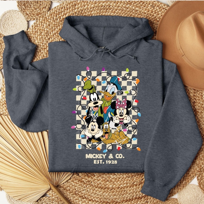 May include: A dark gray hooded sweatshirt with a vintage-style graphic of Mickey Mouse and friends. The graphic features Mickey, Minnie, Donald Duck, Goofy, and Pluto surrounded by colorful Christmas lights. The text "MICKEY & CO. EST. 1928" is printed below the graphic.