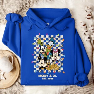 May include: A royal blue hoodie with a graphic of Mickey Mouse, Minnie Mouse, Donald Duck, Goofy, and Pluto surrounded by Christmas lights on a checkered background. The text "Mickey & Co. EST. 1928" is printed below the graphic.