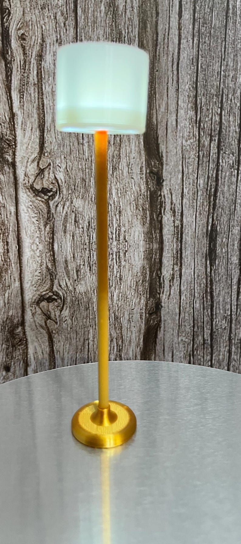 May include: A gold floor lamp with a white cylindrical shade. The lamp is on a silver table.