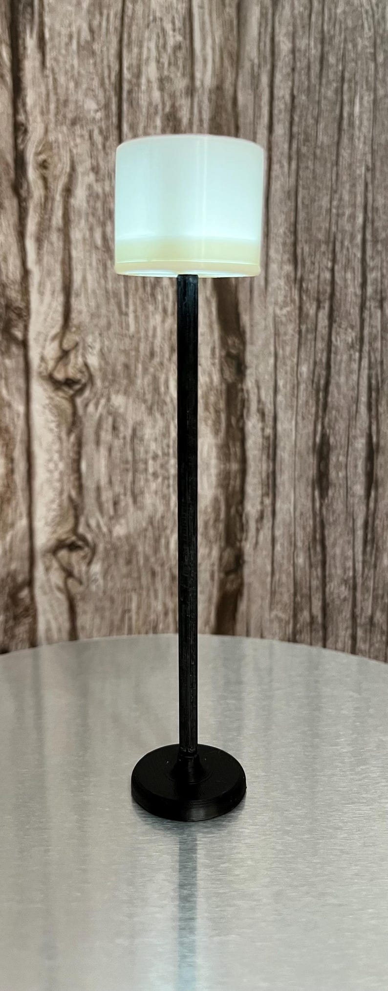 May include: A black floor lamp with a white cylindrical shade. The lamp has a simple design and a black base.