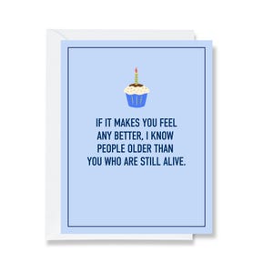 May include: A light blue greeting card featuring a graphic of a single cupcake with a lit candle at the top. The text reads: IF IT MAKES YOU FEEL ANY BETTER, I KNOW PEOPLE OLDER THAN YOU WHO ARE STILL ALIVE. The card has a dark blue border.
