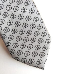 May include: A gray silk tie with a repeating pattern of black camera icons.