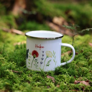 May include: White enamel mug with a floral design and the name "Heike" in red lettering. The mug is sitting on a bed of green moss.