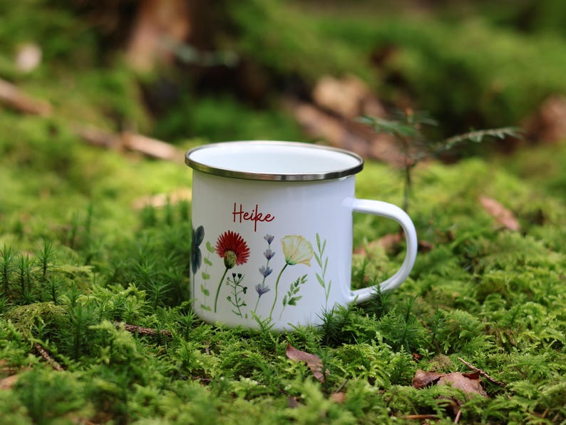 May include: White enamel mug with a floral design and the name "Heike" in red lettering. The mug is sitting on a bed of green moss.
