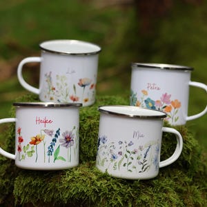 May include: Four white enamel mugs with floral designs and names "Lia", "Heike", "Petra", and "Mia" printed on them. The mugs are sitting on a bed of green moss.