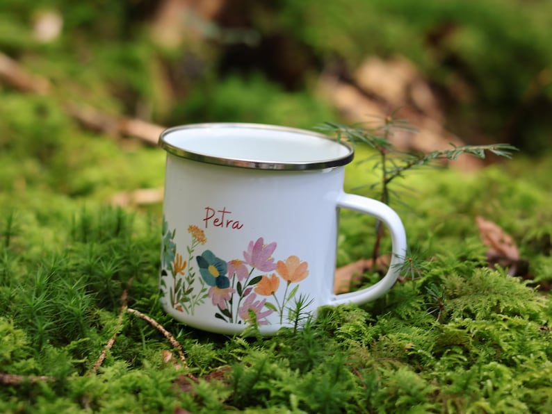 May include: White enamel mug with a floral design and the name "Petra" printed on the front. The mug is sitting on a bed of green moss.