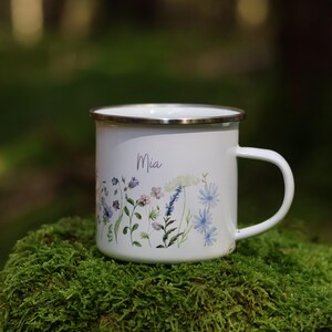 May include: White enamel mug with a floral design and the name "Mia" printed on the front. The mug is sitting on a bed of green moss.